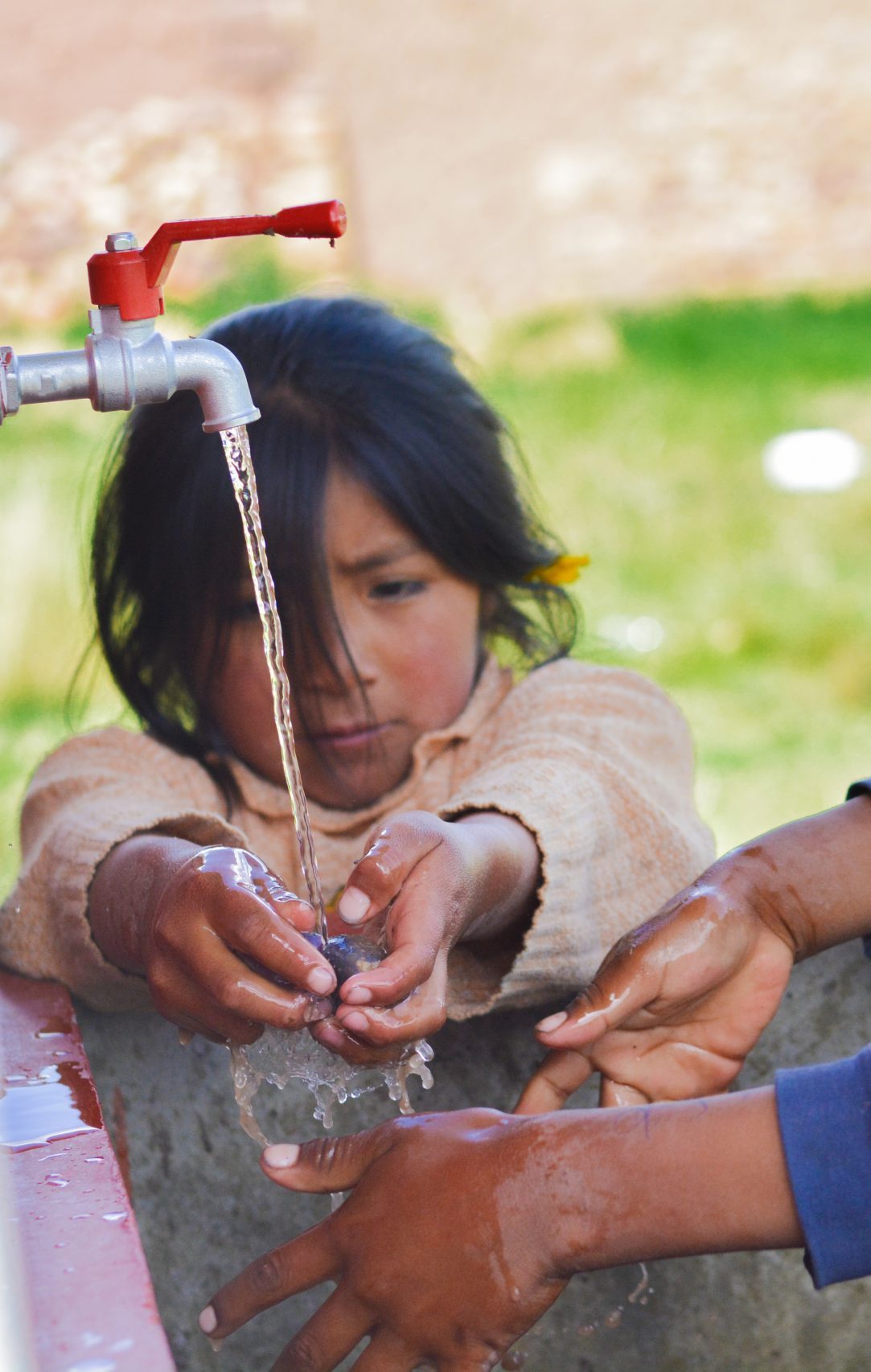 Niña lavándose las manos bajo un grifo al aire libre